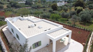 A modern white house with a flat roof, solar panels, and a covered patio area.