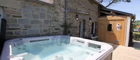 A stone building with a wooden deck, a hot tub, and a sauna.