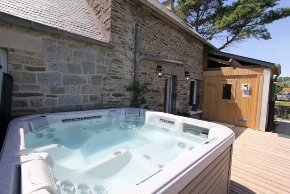 A stone building with a wooden deck, a hot tub, and a sauna.