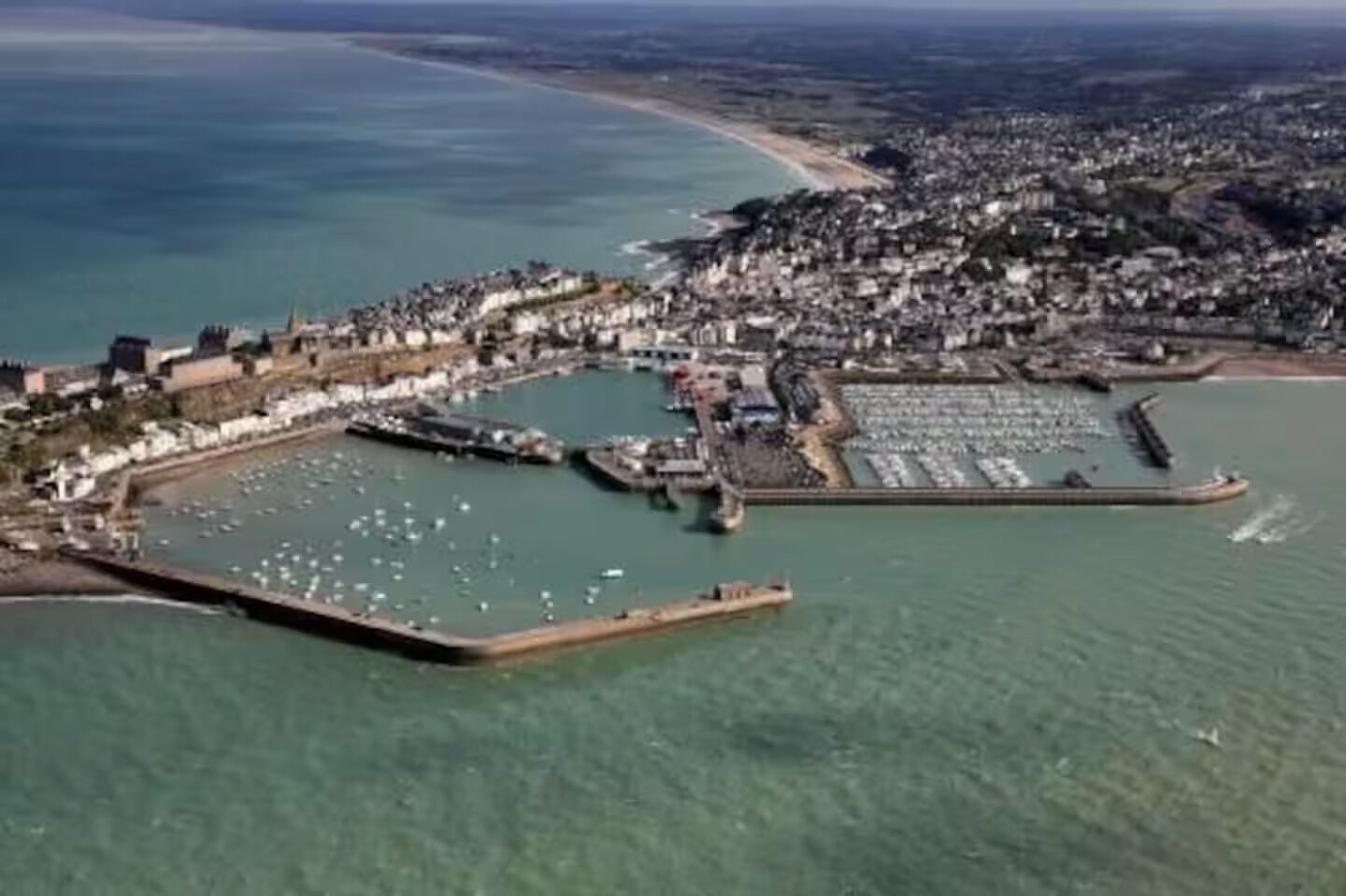 An aerial view of a coastal town with a marina, residential buildings, and a beach.