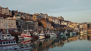 Un port où des bateaux sont amarrés, des bâtiments le long de la rive et un ciel dégagé.