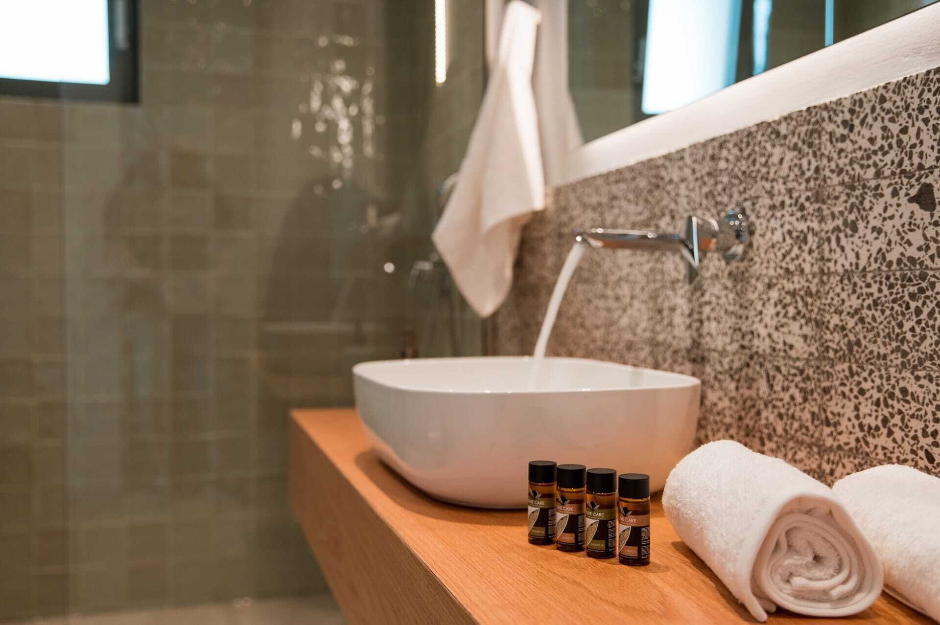 A bathroom with a large white basin, a towel, and three small bottles on a wooden counter.