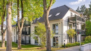 Un immeuble résidentiel moderne à plusieurs étages, doté de balcons, de grandes fenêtres et d’une allée pavée.