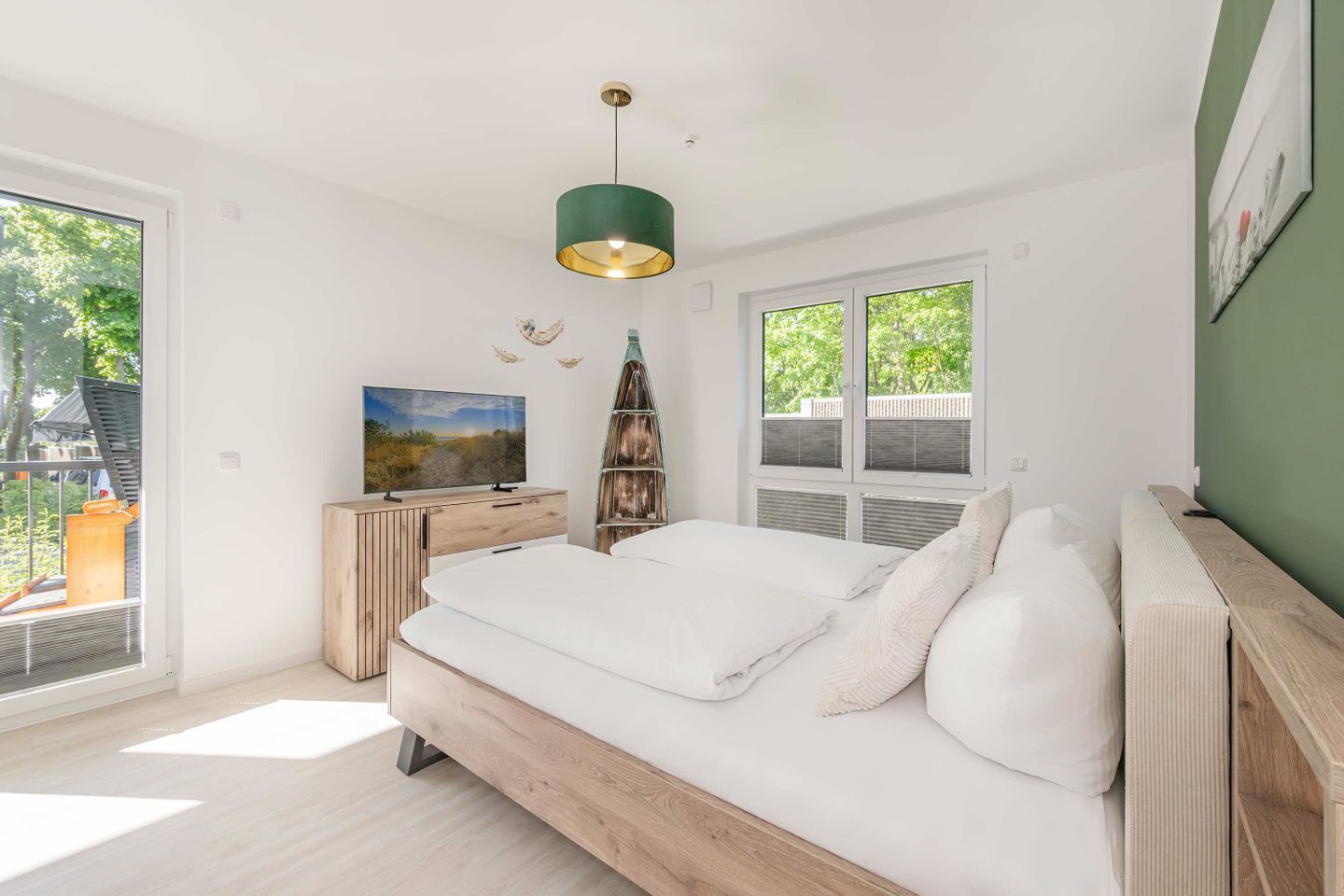 A modern bedroom with a bed, a TV, a wooden dresser, and a large window.