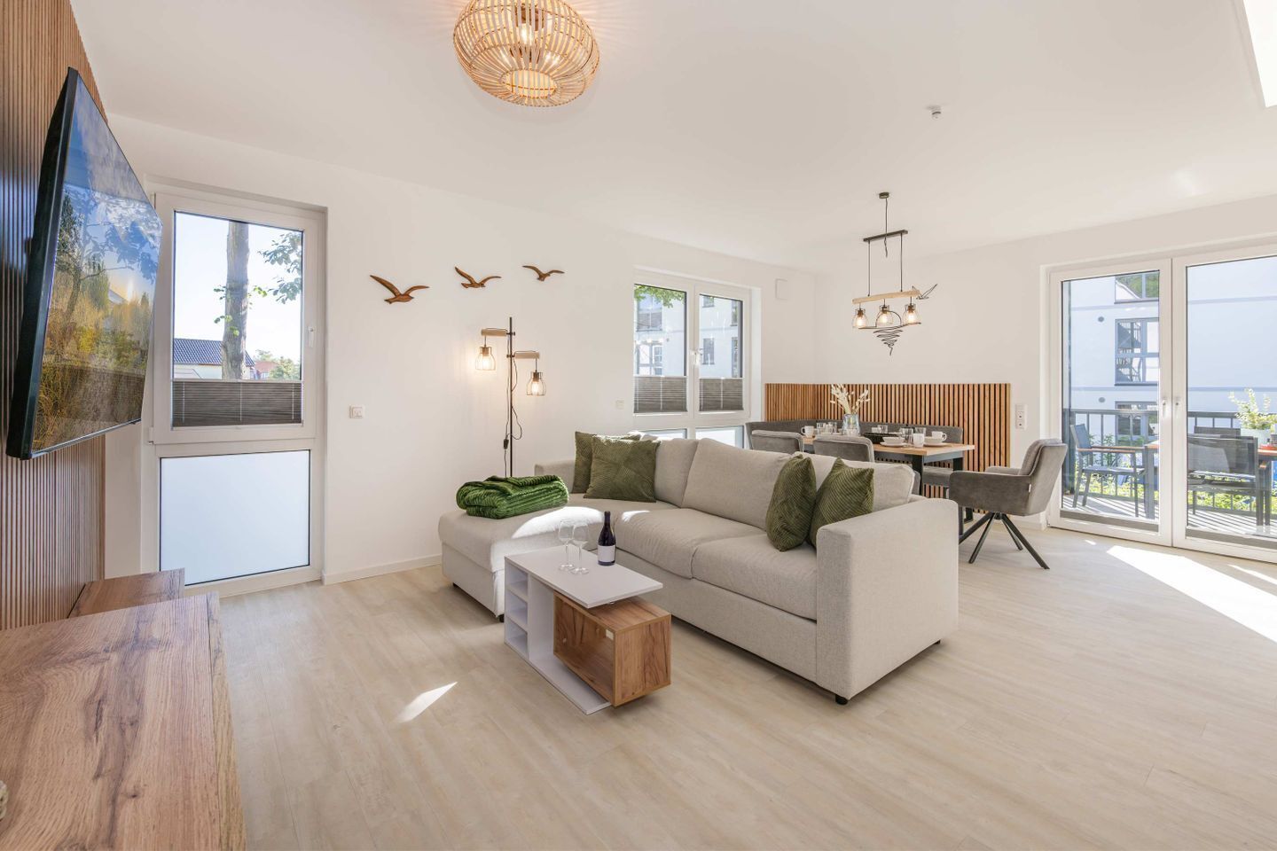 En rummelig opholdsstue med sofa, sofabord og spisebord. Store vinduer, en balkon og en moderne lysekrone.