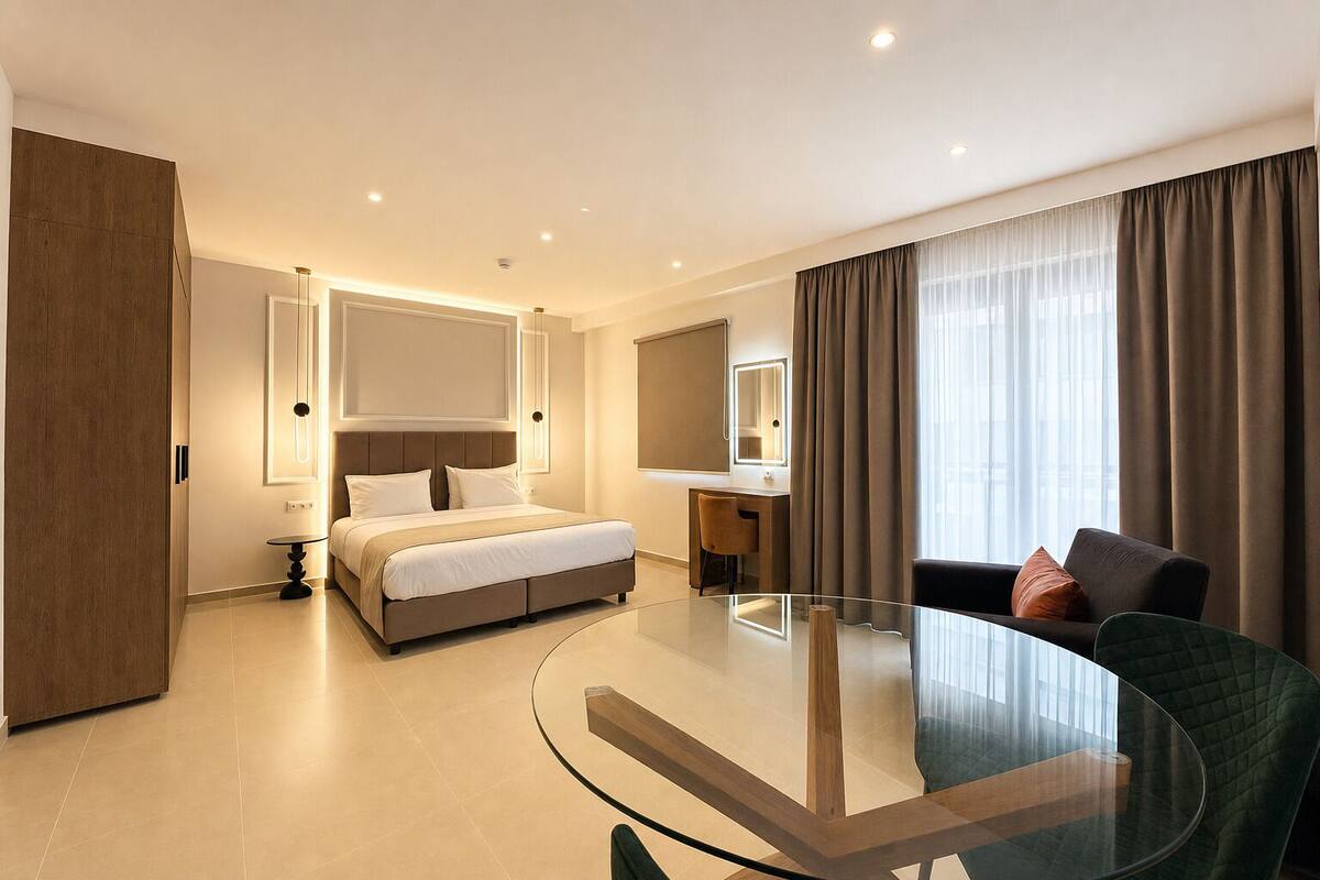 A hotel room with a bed, a desk, a glass table, a sofa, and a large window with curtains.