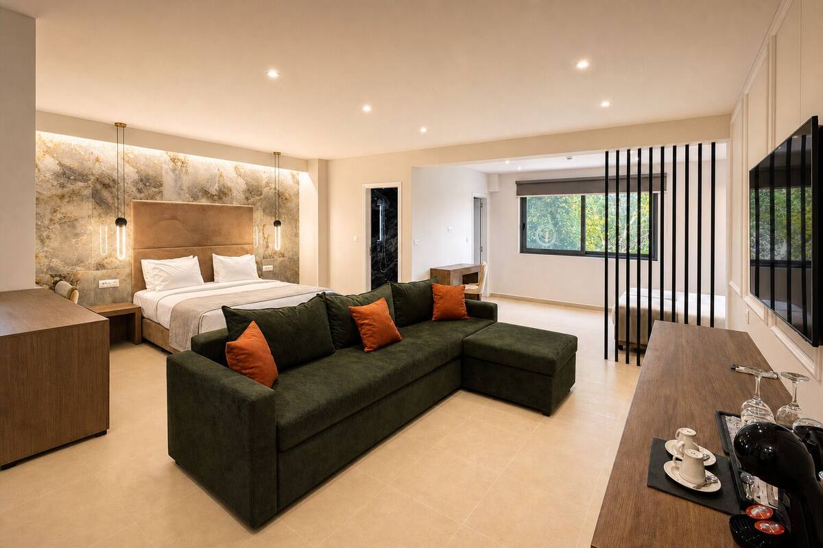 A modern bedroom with a bed, a green sectional sofa, a wooden desk, and a large window.