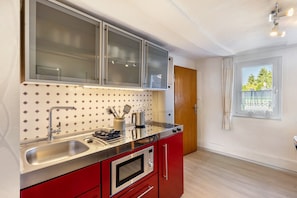 A modern kitchen with a stainless steel sink, red cabinets, a microwave, and a window with a view of trees.