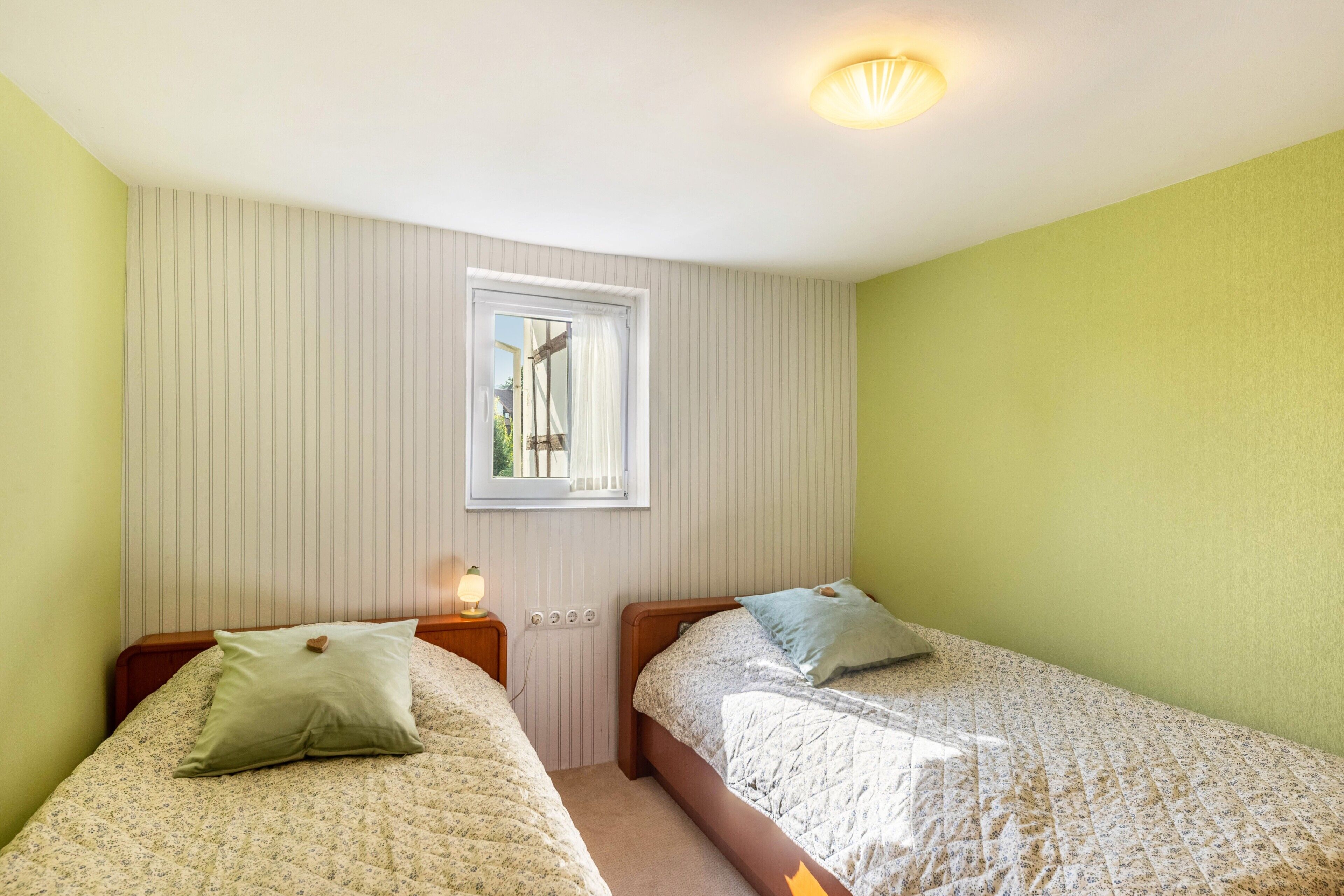 Een kamer met twee bedden, een raam, een lamp en een deur.
