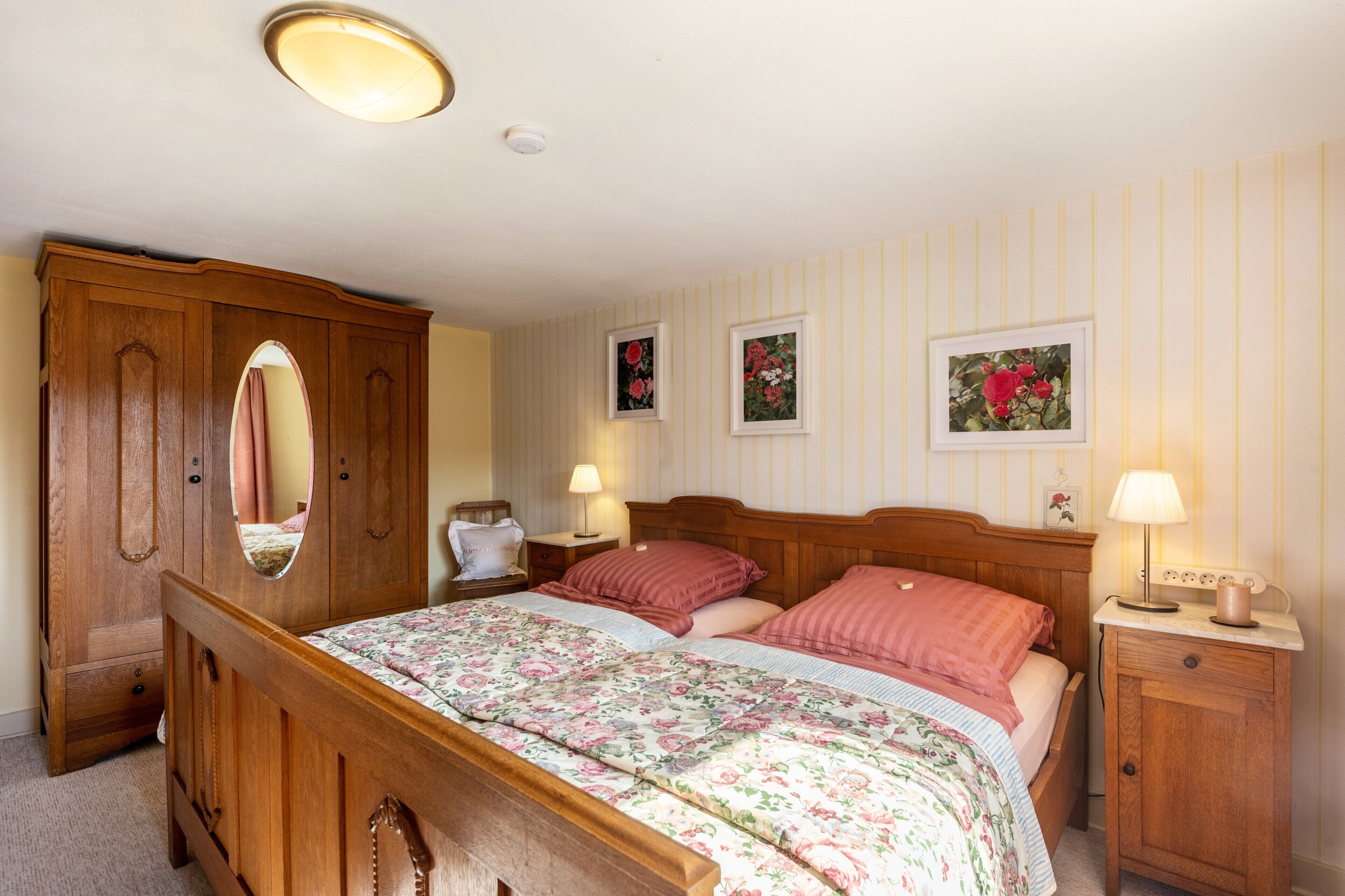 Een slaapkamer met een houten bed, twee nachtkastjes met lampen, een garderobe en bloemenversieringen aan de muur.
