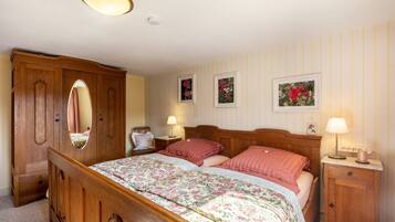 Een slaapkamer met een houten bed, twee nachtkastjes met lampen, een garderobe en bloemenversieringen aan de muur.