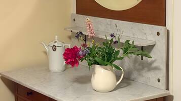 Un meuble-lavabo de salle de bain avec un miroir, un pichet blanc et un arrangement floral.