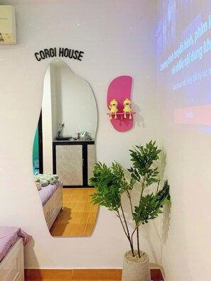 A room with a bed, a desk, a mirror, a potted plant, and a projection screen displaying text. - Corgi House Homestay Nha Trang 3 (Bac Nha Trang)