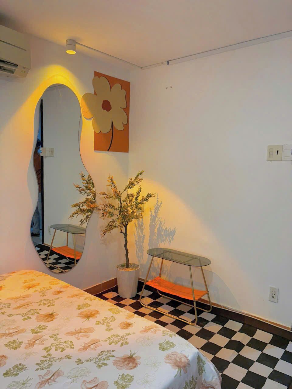 A room with a bed, a chair, a potted plant, and a wall-mounted mirror.