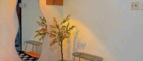 A room with a bed, a chair, a potted plant, and a wall-mounted mirror.