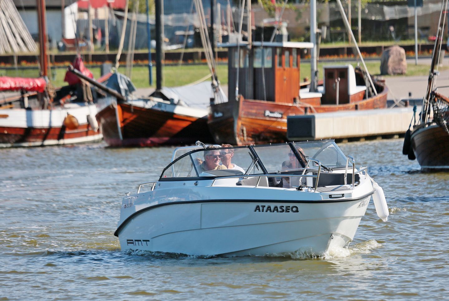 A boat with the name 'ATAASEQ' on its side, moving through water with other boats in the background.