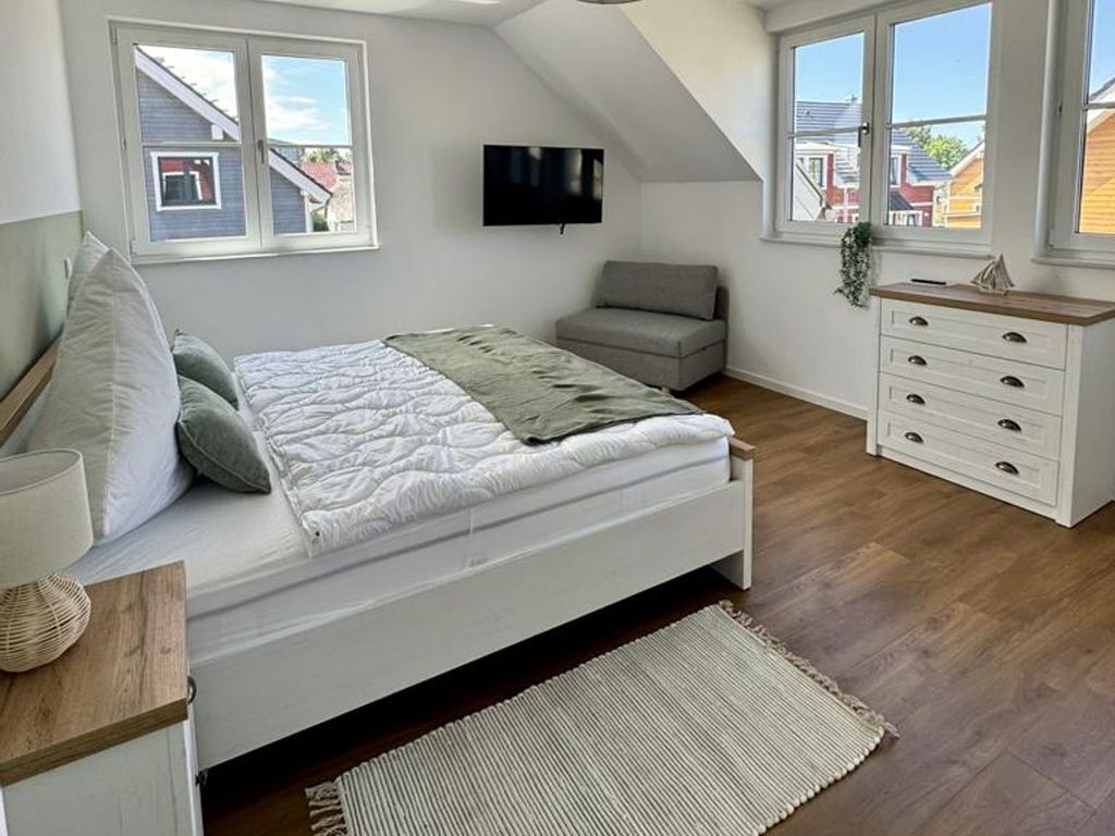 A bedroom with a bed, a TV, a dresser, and a window with a view of houses.