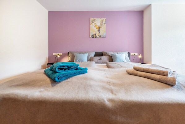 A bedroom with a bed, pillows, a painting on the wall, and a nightstand with a lamp.
