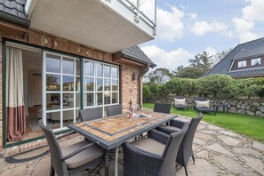 A patio with a table and chairs, a stone wall, and a view of a garden.