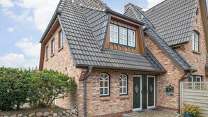 A two-story brick house with a steeply pitched roof, a front entrance with a door, and a small porch area. - Sölring Juwel Whg. 1 - Relaxed living in the Sölring Juwel Whg. 1 in (Wenningstedt-Braderup (Sylt))