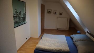 Ein kleines, ordentliches Schlafzimmer mit einem Einzelbett, einem Heizkörper und einem Stadtbild-Poster an der Wand.