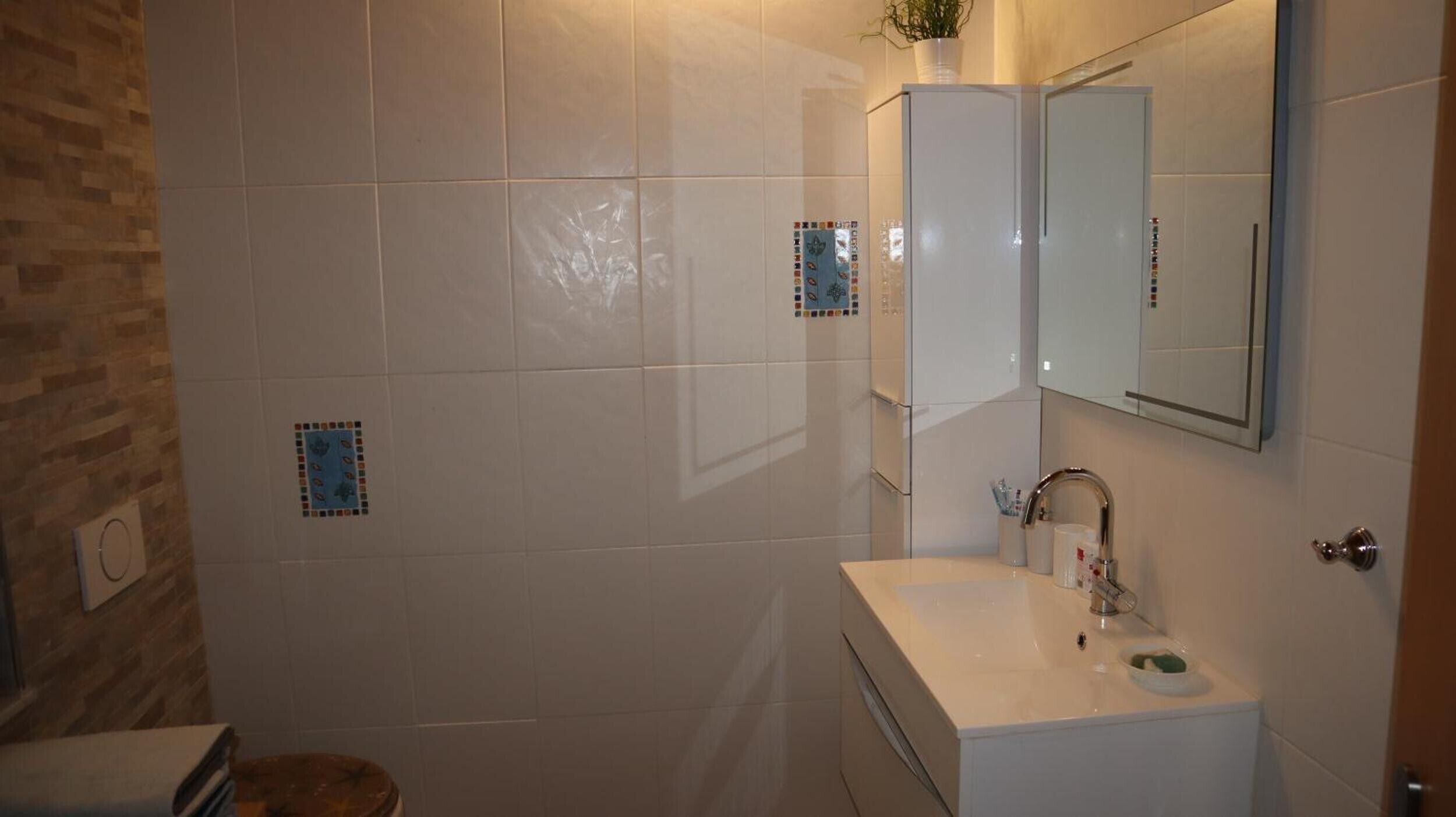A bathroom with a white sink, mirror, and tiled walls.