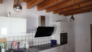 Une cuisine moderne avec des armoires blanches, une hotte noire, un four encastré et un dosseret carrelé.