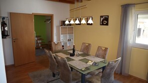 Un coin repas avec une table dressée pour quatre personnes, un mur vert et une fenêtre avec des rideaux.