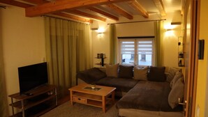 Un salon confortable avec un canapé, une table basse, un téléviseur et une fenêtre avec des rideaux.