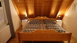 Une chambre avec un plafond en bois, deux lits avec une literie à motifs, des lampes de chevet et une fenêtre avec des rideaux.