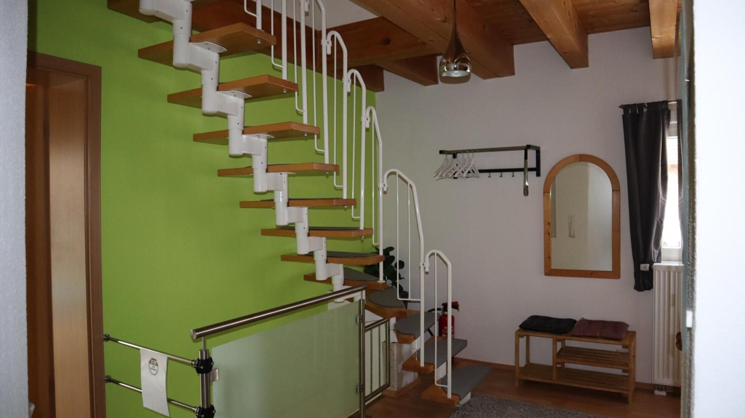 Uma escadaria com corrimãos brancos, um banco de madeira, um espelho e um radiador.