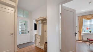 Um corredor com piso de madeira, porta branca, armário para casacos e janela com cortinas.