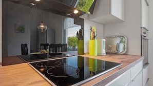 Uma cozinha moderna com ilha de vidro, eletrodomésticos de aço inoxidável e área de refeições com cadeiras e mesa.
