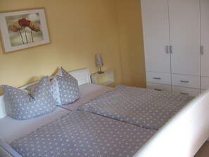 A double bed with patterned bedding, a bedside table with a lamp, a framed picture on the wall, and a wardrobe.