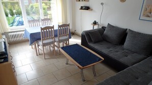 Ein Wohnzimmer mit Sofa, Sesseln, einem kleinen Tisch und Blick ins Freie.