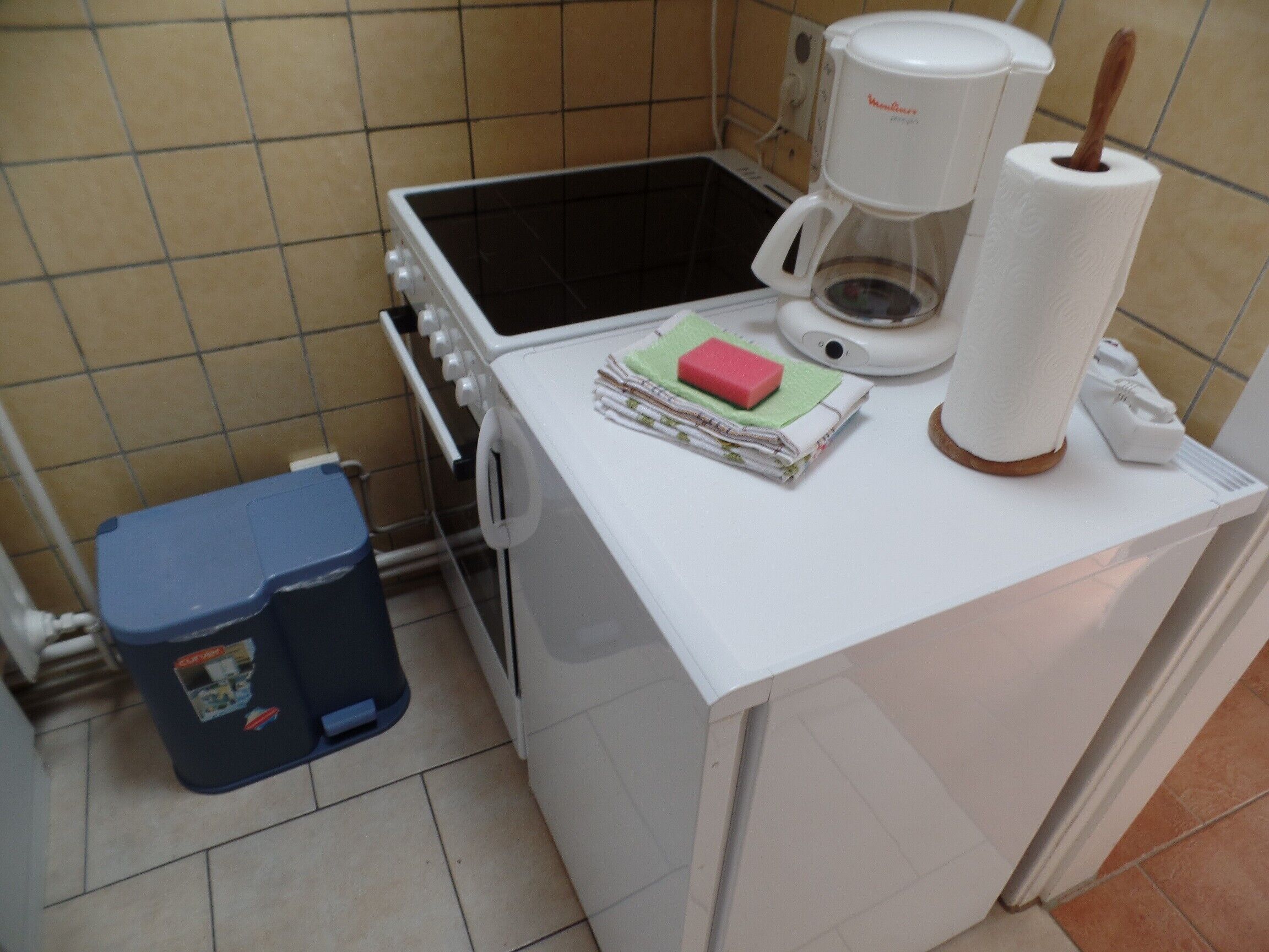 Eine kleine Küche mit Herd, Kaffeemaschine und Mülleimer.