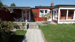 Ein zweistöckiges Haus mit Vorgarten, einer Terrasse mit Stühlen und einem kleinen Garten.
