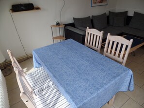 Uma área de refeições com uma mesa coberta por toalha azul, rodeada por cadeiras brancas.
