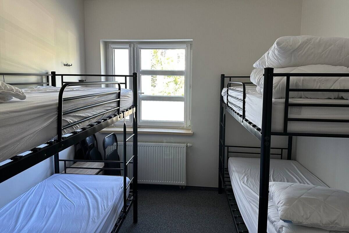 Une chambre de dortoir avec des lits superposés, un radiateur et une fenêtre donnant sur un espace verdoyant.