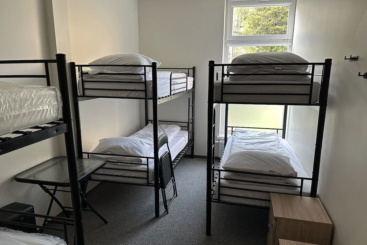 Une chambre de dortoir avec des lits superposés, une petite table et une fenêtre donnant sur les arbres.