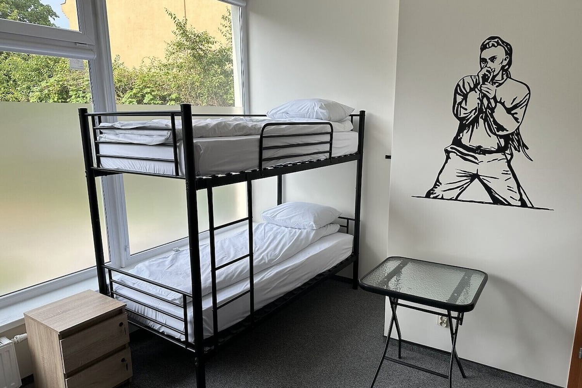 Une chambre avec un lit superposé, une petite table et un radiateur.