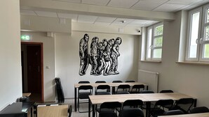 Uma sala de aula com mesas, cadeiras, um projetor e um mural na parede.