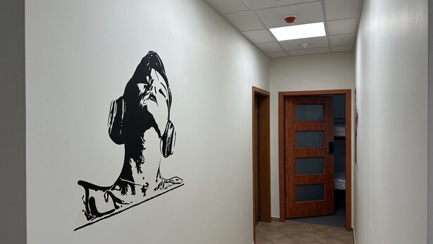 Um corredor com um mural em preto e branco na parede, uma porta de madeira e piso de azulejos.