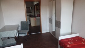 A room with a bed, a desk, a chair, a wardrobe, and a kitchenette in the background. - Apartment '4-Raum Ferienwohnung' with Shared Terrace and Wi-Fi (Cuxhaven)