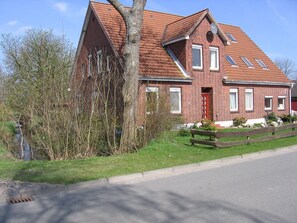 Une maison en briques rouges, avec un toit en pente, une clôture en bois et une cour couverte d’herbe.