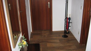 A hallway with wooden flooring, a door, a coat rack with a jacket, and a small plant.