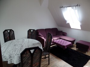 A room with a purple sofa, a small table, and a window with curtains. - Apartment '3-Raum' with Shared Terrace and Wi-Fi (Cuxhaven)
