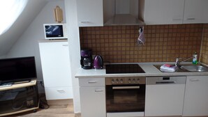A compact kitchen with a microwave, coffee maker, kettle, and a dishwasher.