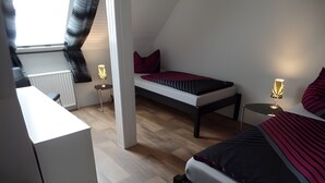 A bedroom with a bed, a desk, a chair, a radiator, and a window with curtains.