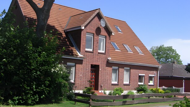 A red brick house with a sloped roof, multiple windows, and a large tree in the foreground.